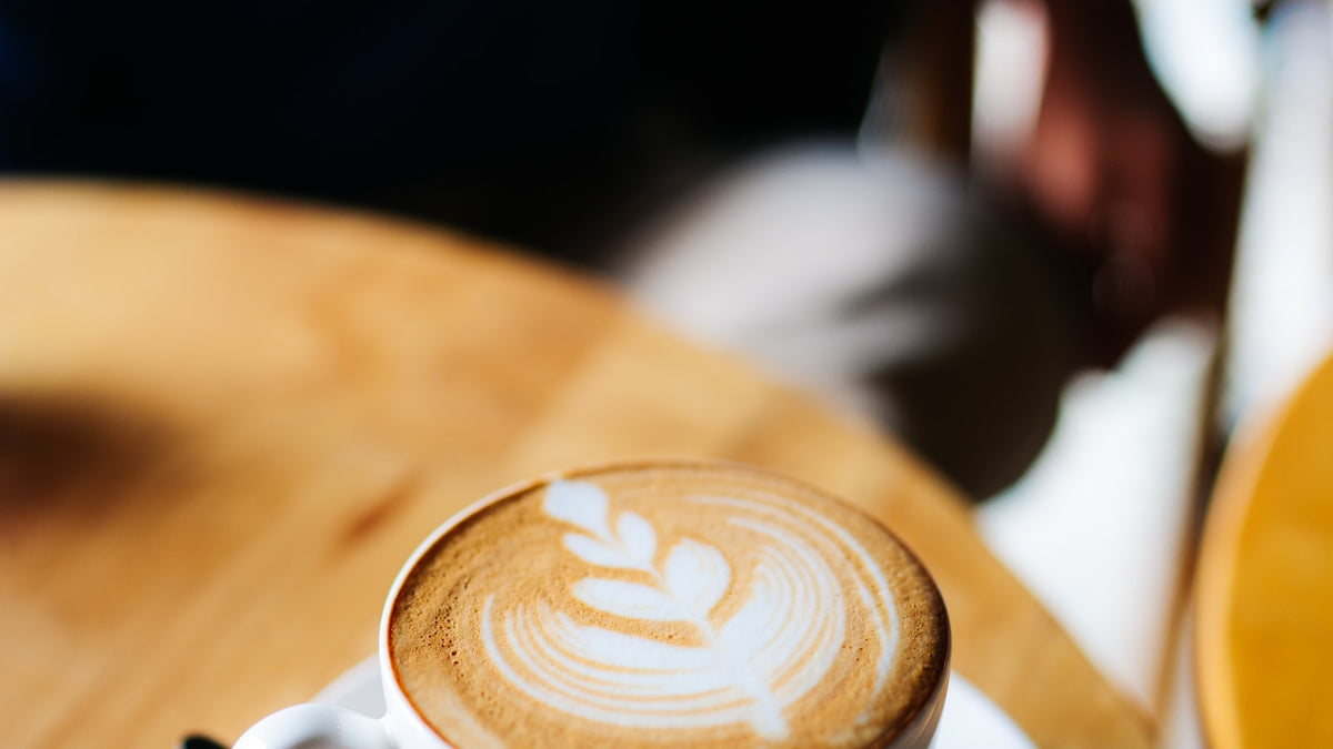 A white ceramic cup of latte with poured art, on a desk