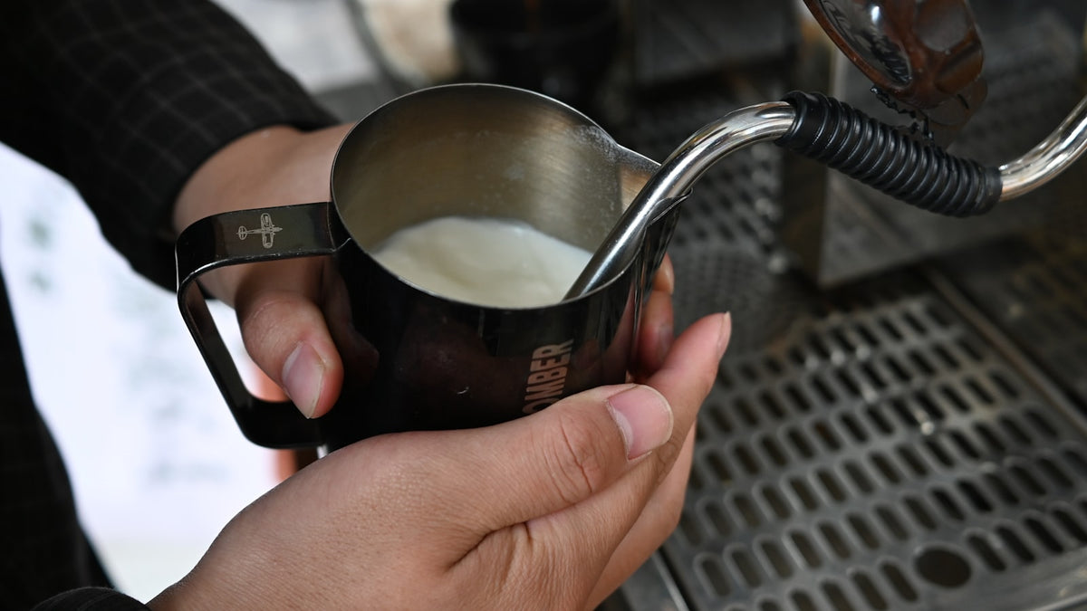 A barista steaming milk in a metal pitcher